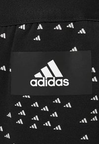 Sort stof med et gentaget hvidt trekantet mønster, med en sort rektangulær lap, der viser den hvide adidas-logo tydeligt.