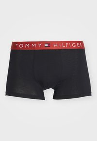 Schwarze Baumwollboxershorts mit rotem elastischem Bund, auf dem der Text "TOMMY HILFIGER" und das Logo zu sehen sind. Glatte Textur mit einer taillierten Passform.