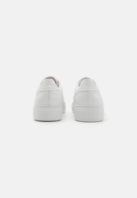 Weiße Leder-Sneaker mit glatter Oberfläche, abgerundetem Absatz, strukturiertem Gummiaußensohle und minimalistischen Design. Ansicht von hinten.