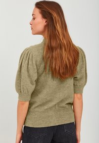 Olivno zelen džemper pleten iz pređe s kratkim napućenim rukavima i rebrastim obrubom, izrađen od mekog, teksturiranog materijala prikladnog za svakodnevno nošenje.