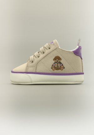 Beige tumlingsneaker med lilla kant, snørebånd og en lille broderet teddybjørn med hat på siden.