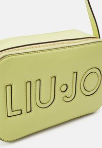 Sac bandoulière Liu Jo en cuir vert clair avec détail de logo découpé, fermeture éclair dorée et contours en brun contrastant.