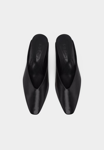 Ζευγάρι μαύρα δερμάτινα μύταυλα με χαμηλό τακούνι, φωτογραφημένα από ψηλά σε λευκό φόντο.