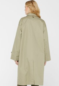 Langmantel in hellolivgrün mit entspanntem Schnitt, abgesenkten Schultern und glatter Textur. Beinhaltet einen Rückenschlitz für mehr Bewegungsfreiheit.