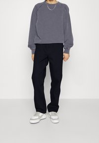 Szary sweatshirt z raglanowymi rękawami, w połączeniu z ciemnymi spodniami. Białe sneakersy z szarymi akcentami. Minimalistyczny design i miękka tekstura.