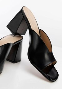 Zwarte leren blokhak mules met een open teen en een V-vormig ontwerp. Glad textuur met een effen kleur en minimale hardware details.