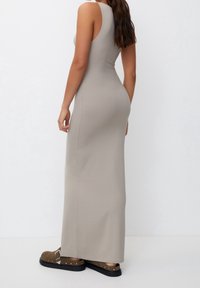 Robe maxi sans manches, ajustée, en tissu beige doux avec une texture lisse, associée à des sabots marron ornés de clous sur la lanière et la semelle.