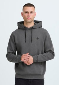 Felpa grigia con cappuccio realizzata in tessuto morbido. Presenta un cappuccio regolabile con lacci, tasca anteriore e un piccolo logo sul petto. Polsini aderenti.