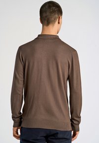 Ruskea neulottu pitkähihainen poolopaita, jossa on ribbireunat kauluksessa ja hihoissa. Ominaisuuksiin kuuluu sileä pinta ja siistit linjat, ja se on suunniteltu istuvaksi.