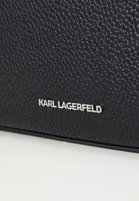 Borsa a tracolla in pelle nera con texture, caratterizzata da un logo argentato, una finitura a ciottoli e una silhouette strutturata.