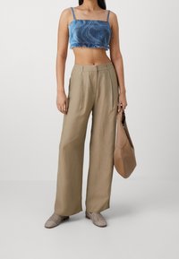 Top de denim azul recortado con un patrón ondulado, combinado con pantalones de pierna ancha en marrón claro, zapatos beige texturizados y un bolso marrón.