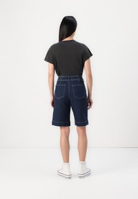 T-shirt cinza escuro e calções de ganga escuros até ao joelho com barras dobradas, apresentando dois bolsos traseiros e ténis brancos.