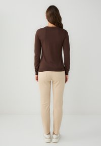 Een bruine, lang mouw fitted trui, beige slim-fit broek en witte sneakers. Soepele textuur, eenvoudig ontwerp, met achterzakken op de broek.