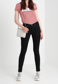 Červeno-bílé pruhované tričko s černými džíny. Stříbrné tenisky a malá bílá taška přes rameno. Slim fit s kulatým výstřihem.