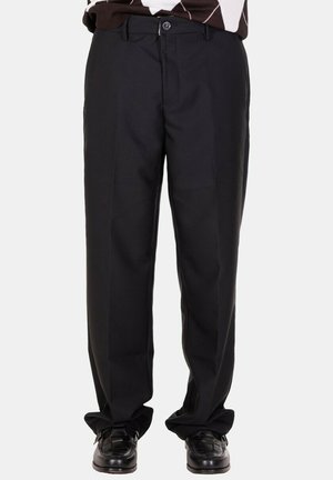 Pantaloni neri dritti indossati con scarpe di pelle nere, abbinati a un top marrone e bianco a fantasia, mostrati su uno sfondo chiaro uniforme.