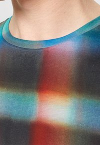 Le haut à manches courtes présente un dégradé multicolore dans des tons de bleu, rouge et noir, avec une texture douce et lisse et un col rond.