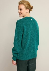 Türkisfarbener Pullover mit strukturiertem Finish, weiten Ärmeln und geripptem Saum. Auf der Rückseite des Halsausschnitts befindet sich ein silberner Sternakzent.