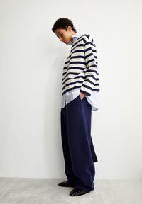 Suéter de algodón a rayas en navy y crema sobre una camisa azul clara, combinado con pantalones de pierna ancha navy y mocasines negros con tachuelas.