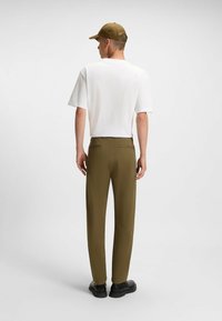 Witte kortemouwen shirt, olijfgroene broek, zwarte schoenen. Eenvoudig, recht gesneden; casual ontwerp met achterzakken en minimale details.