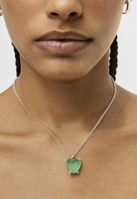 Collana in argento con ciondolo a forma di cuore in pietra verde, adornato da quattro accenti in argento agli angoli, indossata sulla pelle nuda.