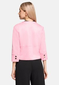 Veste courte rose clair en tissu lisse, dotée de manches trois-quarts et d'accents de boutons noirs sur les poignets. Vue arrière présentée.