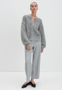 Grau-flauschige Zip-Up-Strickjacke mit Rundhalsausschnitt, kombiniert mit hellgrauen weiten Hosen und schwarzen flachen Schuhen. Glatte Textur und lässige Passform.