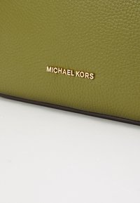 Bolso de mano de cuero texturizado en verde oliva con la marca dorada "MICHAEL KORS". Presenta un borde oscuro liso a lo largo del borde inferior.