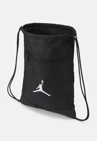 Mochila preta com cordões feita de tecido durável. Possui um bolso com zipper e um logotipo Jumpman em branco. Textura suave com bordas arredondadas.