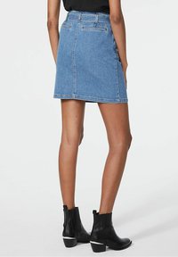 Džínová sukně s přesně padnoucím pasem, světle modré barvy, délky po kolena, design s pěti kapsami a viditelnými švy, doplněná černými kotníkovými botami.