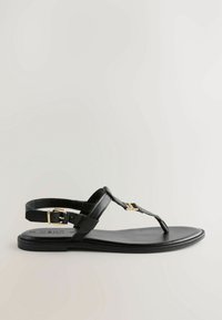 Sandal de plana de cuero negro con diseño de thong, correa ajustable en el tobillo con herrajes dorados y una suela plana y suave.