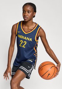 Μπλούζα μπάσκετ σε σκούρο μπλε με τη λέξη "INDIANA" και τον αριθμό "22" σε κίτρινο, με V-λαιμόκοψη και πολύχρωμες λεπτομέρειες. Μαύρο σορτς με λευκές ρίγες.