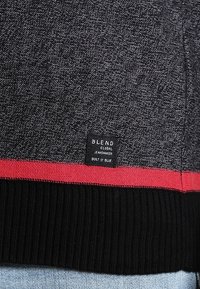Grau strukturierter Pullover mit schwarz geripptem Saum und rotem Streifen. Auf der Seite befindet sich ein „BLEND“-Markenetikett. Lässiges Design.