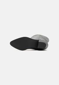 Chaussure en tissu gris avec un bout rond et une semelle en caoutchouc noir lisse, présentant un motif texturé subtil sur le dessus.