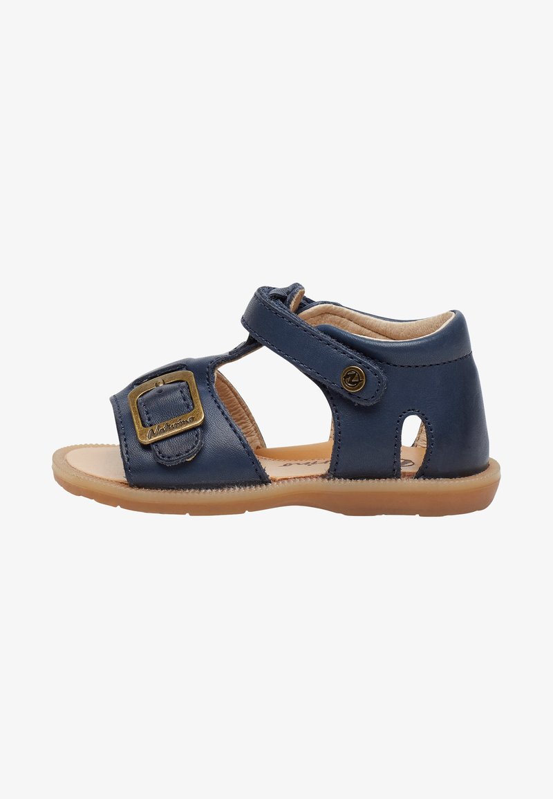 Sandal in pelle blu navy con fibbia laterale, punta aperta e dettagli intagliati. Presenta una suola marrone chiaro e una morbida fodera interna.