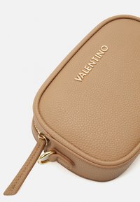 Dzeltenās ādas soma ar teksturētu apdari, zelta aparatūra un iegravēts "Valentino" logotips uz vāka. Zippera aizdare ar ādas siksniņu.