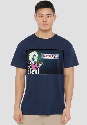 Young man wearing a navy blue T-shirt with a graphic of Beetlejuice character holding a cockroach and the text "BEETLEJUICE."