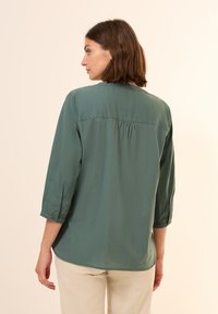 Langarm-Bluse in Waldgrün mit einem Knopfmanschette, plissiertem Rückendetail und glattem Stoff. Geformter Saum und lockere Passform.