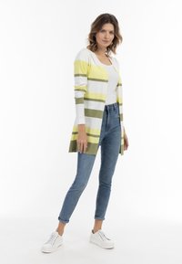 Cardigan a rayas en blanco, amarillo y verde oliva, de manga larga, con apertura frontal, combinado con jeans ajustados blue y zapatillas blancas.