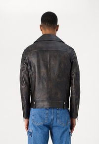 Svart skinnjacka med en något sliten finish, breda slag och dragkedjor vid ärmsluten. Har en figursydd design med bakseams.