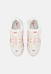 Białe sportowe buty z siateczki i materiału syntetycznego. Posiadają czerwone logo Nike, czarne akcenty i wielokolorowe detale po bokach.