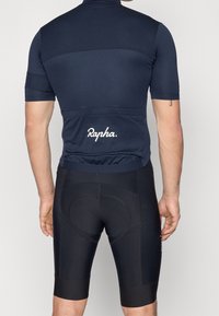 Maillot de ciclismo azul marino con mangas cortas, diseño texturizado y logo blanco "Rapha"; combinado con pantalones cortos de ciclismo acolchados negros.