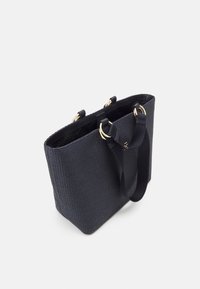 Sac fourre-tout noir texturé avec doubles poignées attachées par des anneaux dorés sur fond blanc.