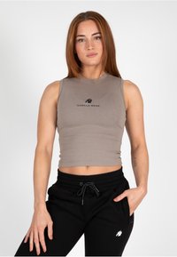 Grijze mouwloze crop top met een aangesloten ontwerp, voorzien van een zwart "GORILLA WEAR" logo. Gecombineerd met zwarte joggerbroeken met zakken.