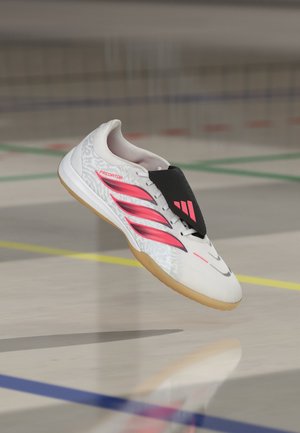 Weißer und rosa Hallenfußballschuh mit Gummisohle und schwarzer Schnürsenkel-Überdeckung, schwebt über einem polierten Hallenboden mit farbigen Spielfeldlinien.