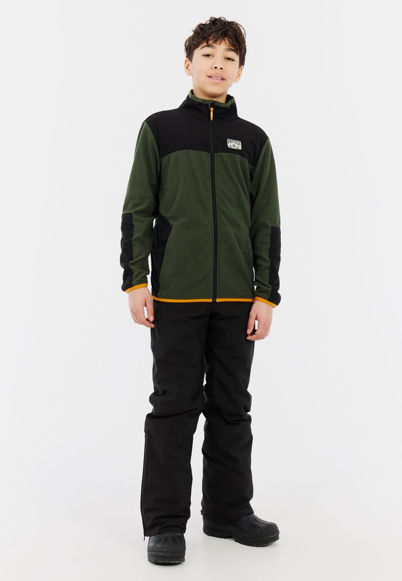 Fleecejack met een donkergrijze en zwarte kleur, voorzien van een rits aan de voorkant, hoge kraag en oranje accenten. Gecombineerd met zwarte waterdichte broek en laarzen.