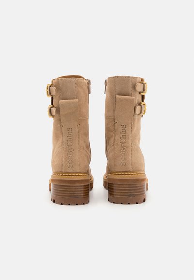 Bottines en daim beige à talons carrés, dotées de deux sangles réglables, d'une fermeture éclair et d'un logo embossé sur le côté.