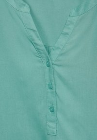 Türkises Shirt mit V-Ausschnitt, drei Knöpfen und einer glatten, weichen Textur mit einem dezenten Glanz.