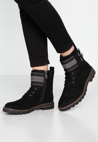Stivali alla caviglia in suede nero con un risvolto in tessuto a righe, chiusura con lacci sul davanti, zip laterale e suola in gomma texturizzata. Ideali per un look informale.