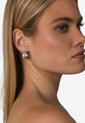 Silberfarbene Creolen mit verschlungenem Design, glatter Oberfläche und klaren Kristallen entlang einer Kante.