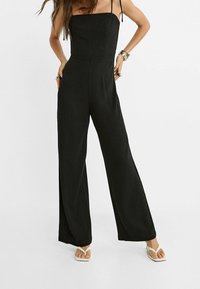 Zwarte linnen jumpsuit met spaghettibandjes, wijde pijpen en een aansluitend lijfje. Soepele textuur en minimalistisch ontwerp.